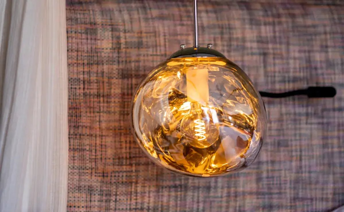 A stylish pendant light with a round glass shade, illuminating a warm glow, hanging from a modern ceiling fixture against a textured background.