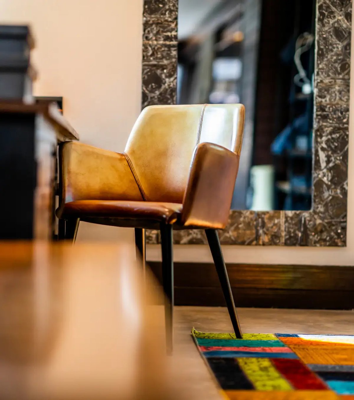 This image features a stylish chair with a mix of tan and brown leather, set against a backdrop of a decorative mirror and a vibrant rug characteristic of a lodge interior.
