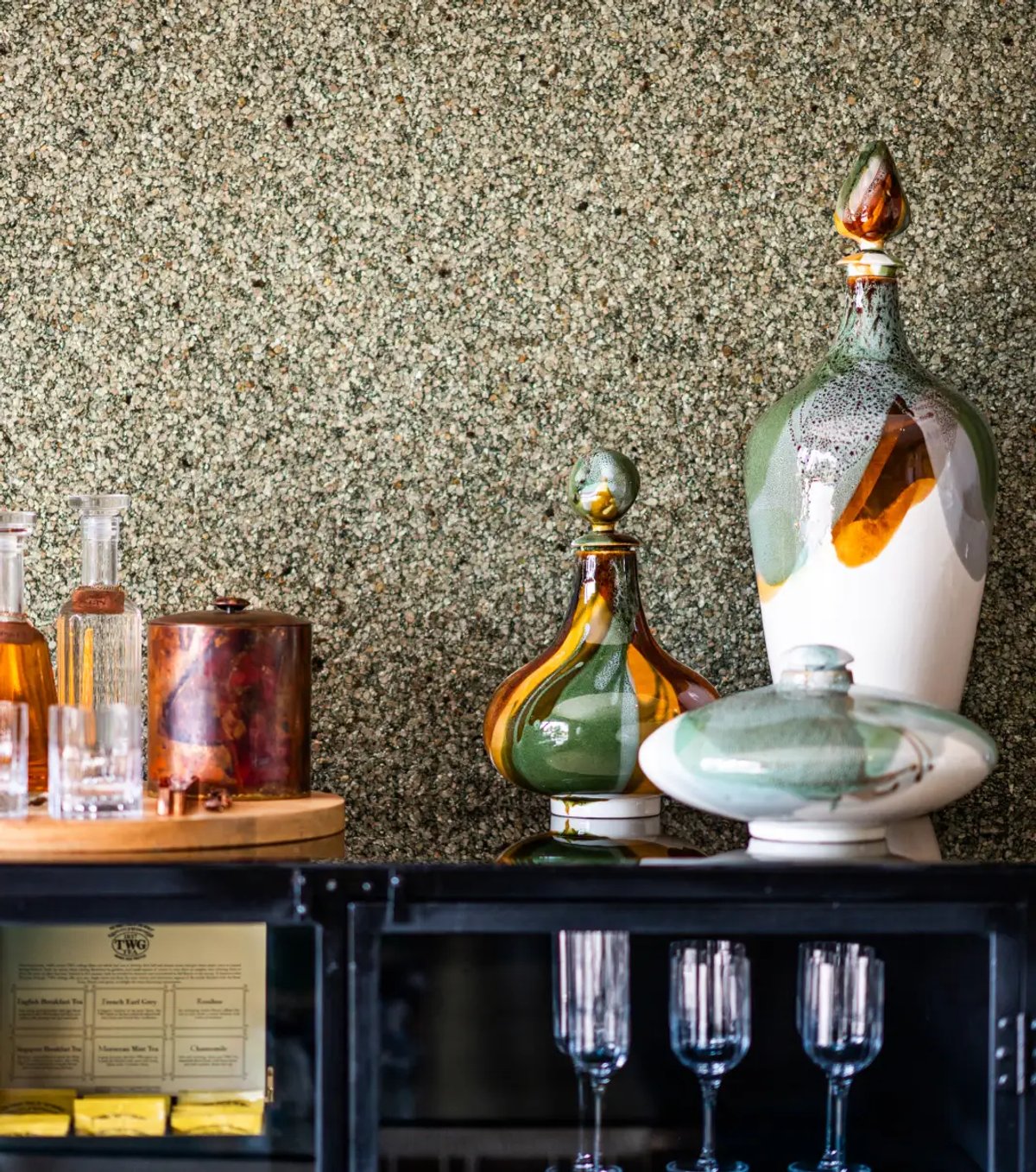 The image features an elegant display of decorative glass items against a textured wall, showcasing various styles and colors.