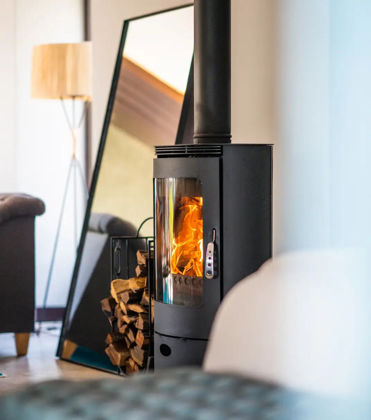 The image showcases a modern interior with a contemporary fireplace, exhibiting flames and surrounded by wood logs, alongside a large mirror reflecting the space.