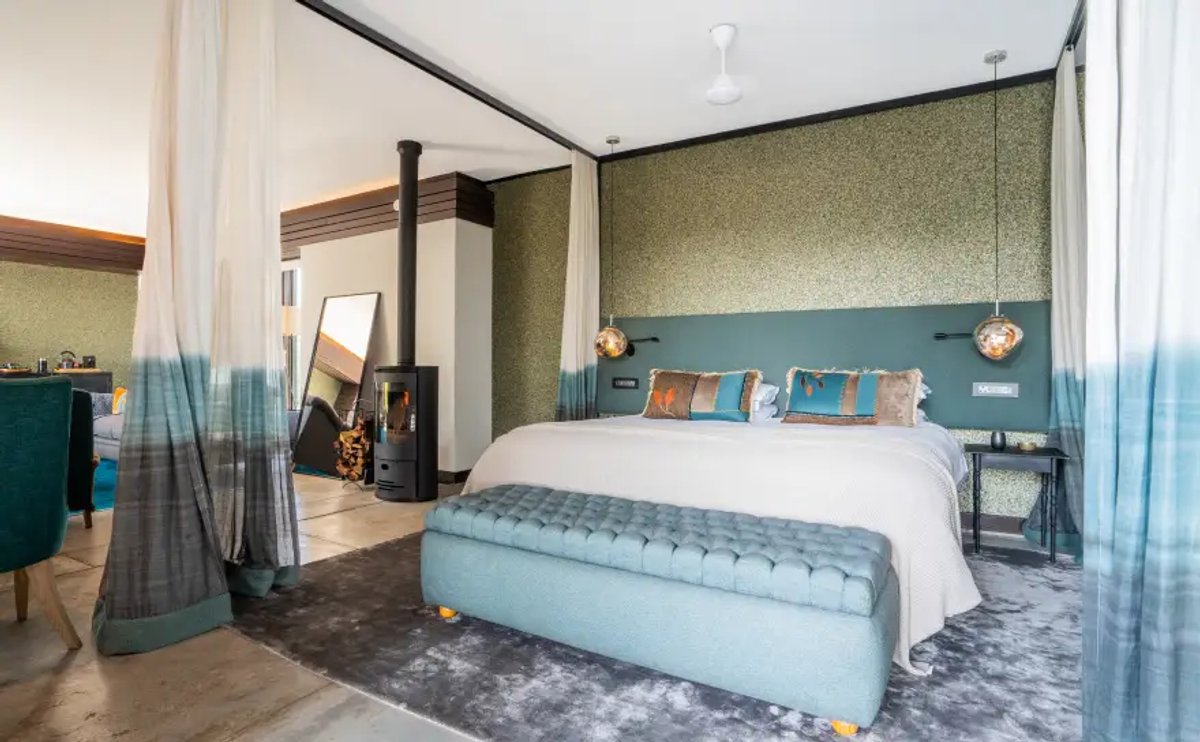 The image showcases a modern room interior at Silvan Safari, featuring a comfortable bed, decorative pillows, and stylish furnishings, along with a cozy fireplace.